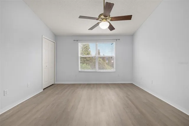 an empty room with wooden floor ceiling fan and windows