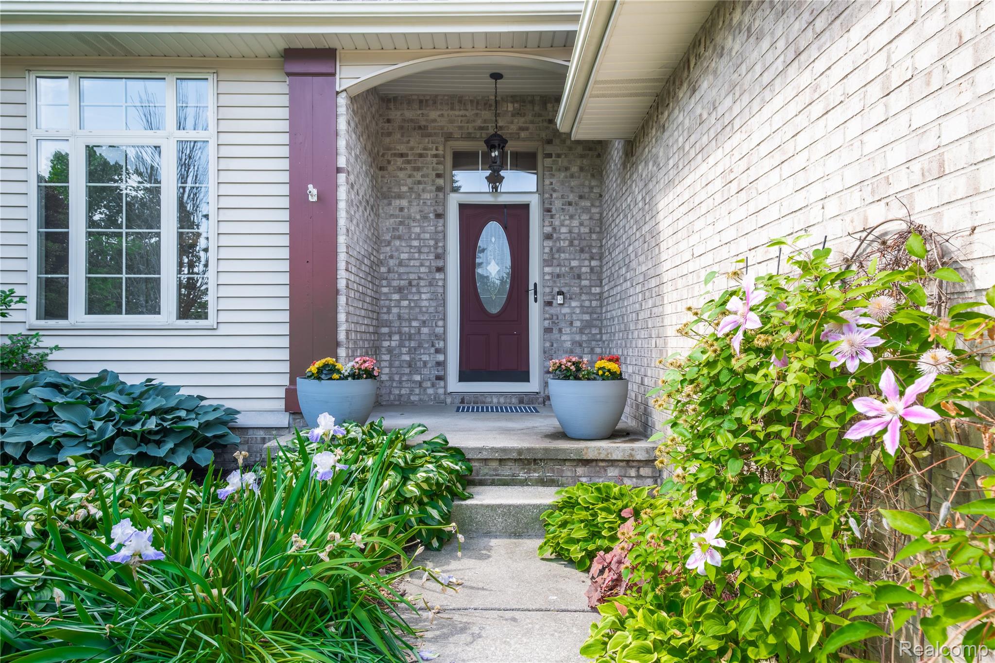 Inviting entryway featuring a red front door with an oval glass insert, a covered porch, and light brick siding