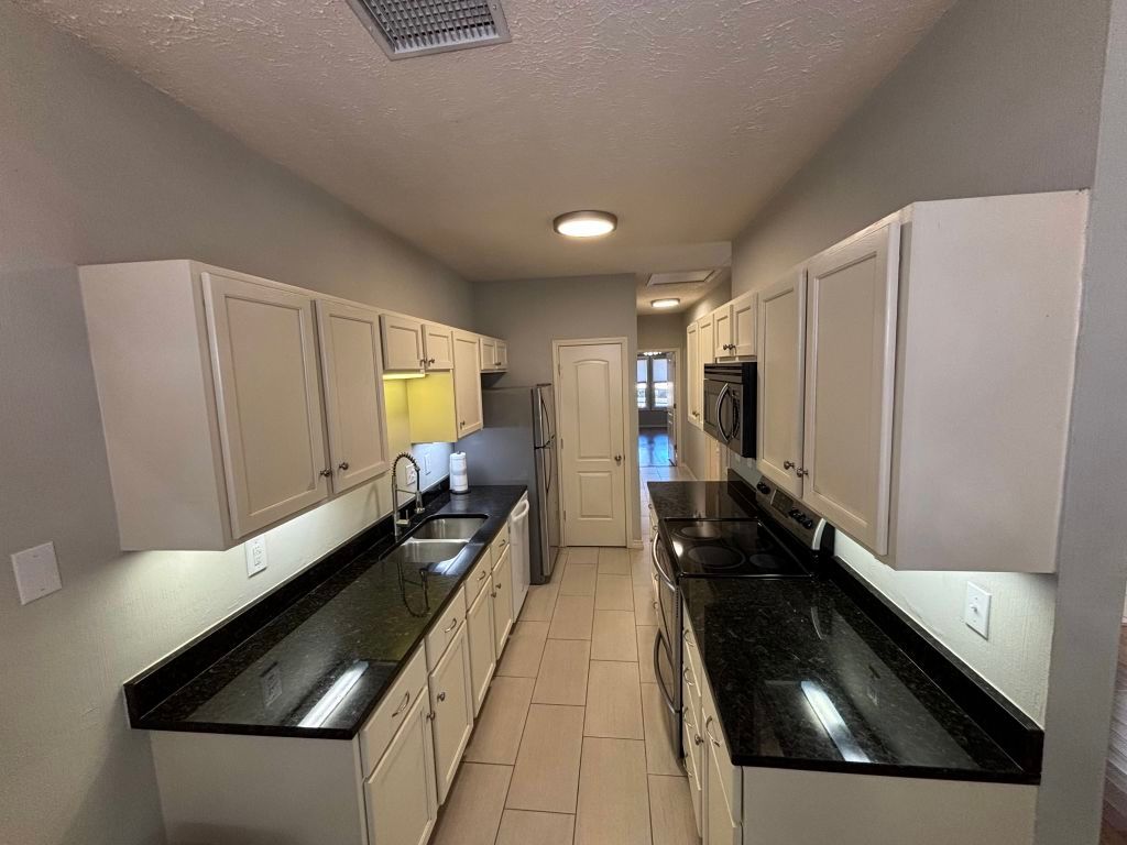307 Quarry Street San Marcos, TX 78666 - Photo 10 of 38 Kitchen with stainless steel electric range oven, a textured ceiling, white cabinets, light tile patterned floors, and dark stone counters