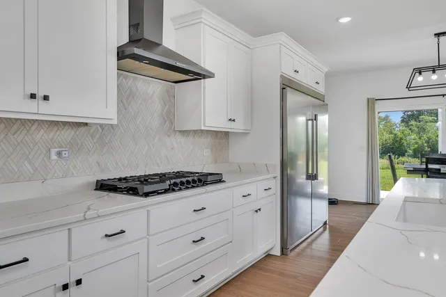 a kitchen with stainless steel appliances granite countertop a stove a sink and white cabinets with wooden floor
