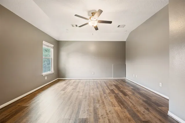 an empty room with wooden floor fan and windows
