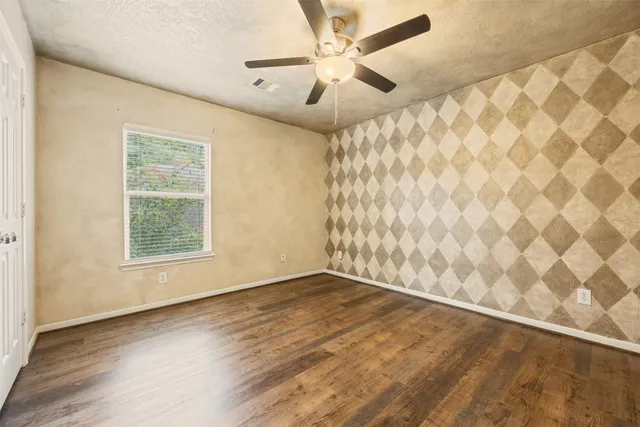 an empty room with wooden floor fan and windows