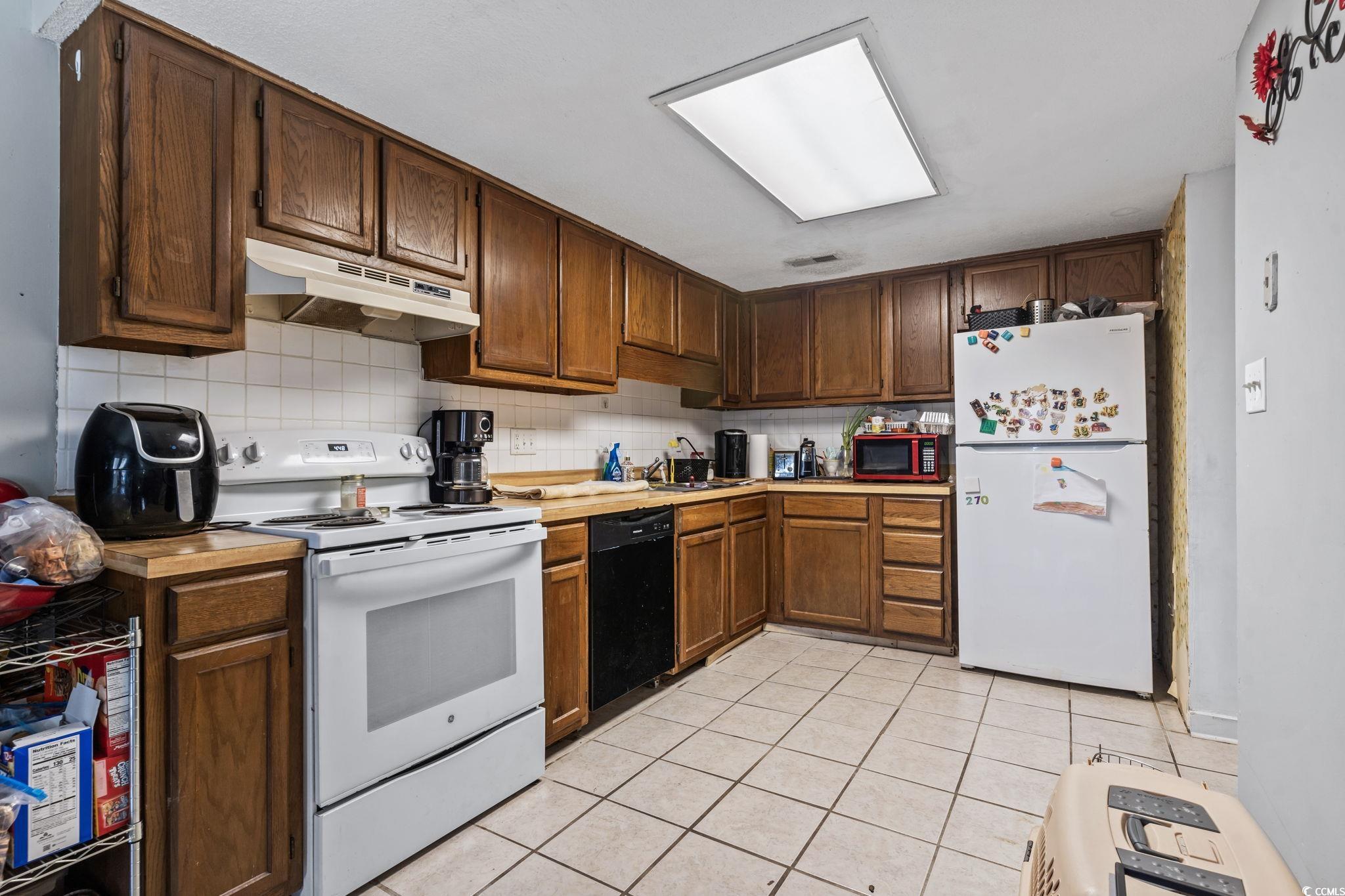 1411 Turkey Ridge Road, Unit 30B Surfside Beach, SC 29575 - Photo 5 of 21 Kitchen featuring backsplash, white appliances, light countertops, under cabinet range hood, and light tile patterned floors