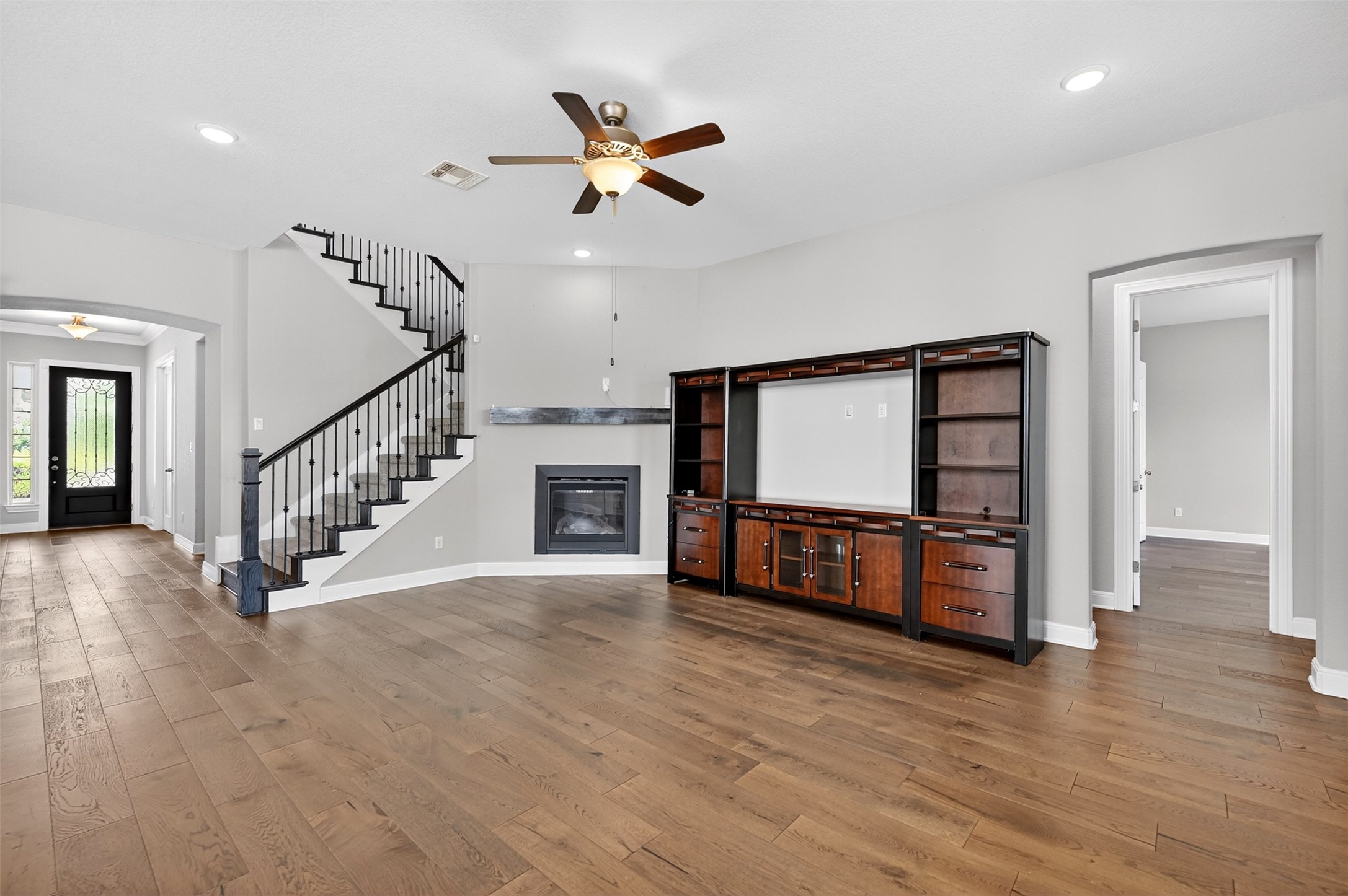 1201 Positano Pass Leander, TX 78641 - Photo 22 of 40 Spacious living area featuring wood-finish flooring, a built-in media center, a fireplace with a wood mantle, a staircase with wrought iron balusters, and recessed lighting
