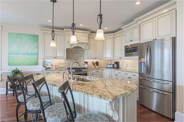 a kitchen with stainless steel appliances granite countertop a refrigerator a sink dishwasher a stove and a dining table with wooden floor