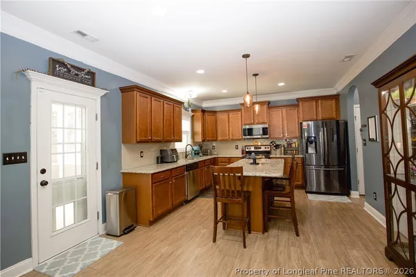 a kitchen with stainless steel appliances kitchen island granite countertop a refrigerator a stove a sink a dining table and chairs with wooden floor