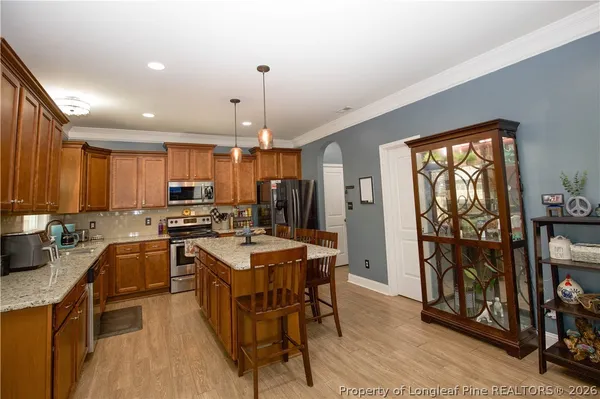 a kitchen with stainless steel appliances granite countertop a refrigerator a sink dishwasher a stove and a dining table with wooden floor
