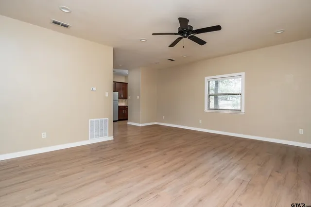 an empty room with wooden floor ceiling fan and windows