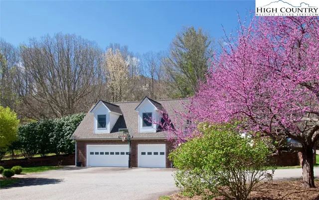 a sign that is sitting in front of a brick house with large trees