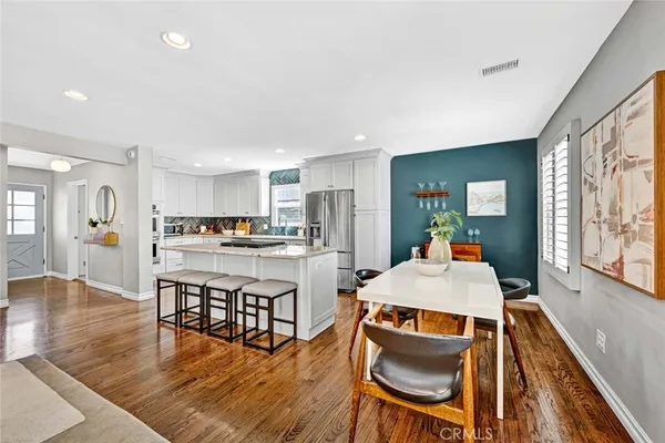 a living room with stainless steel appliances furniture a dining table and kitchen view with wooden floor