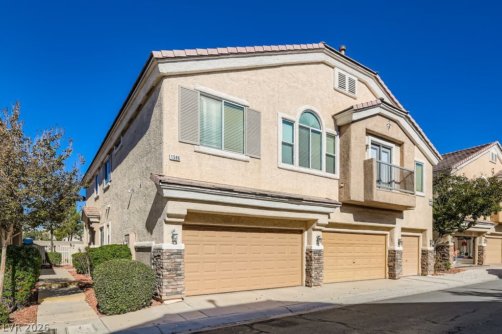 Multi-story residence featuring stucco and stone veneer, multiple garage bays, and a charming balcony.