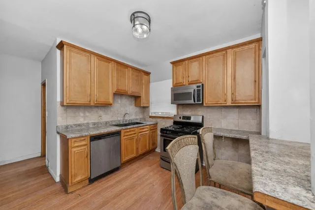 a kitchen with stainless steel appliances granite countertop a stove top oven a sink dishwasher a dining table and chairs with wooden floor