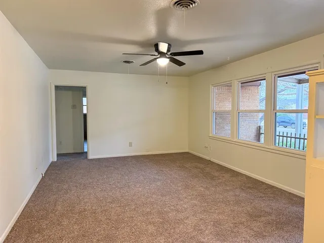 an empty room with chandelier fan and windows