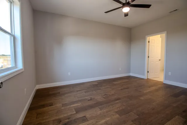 an empty room with wooden floor fan and windows