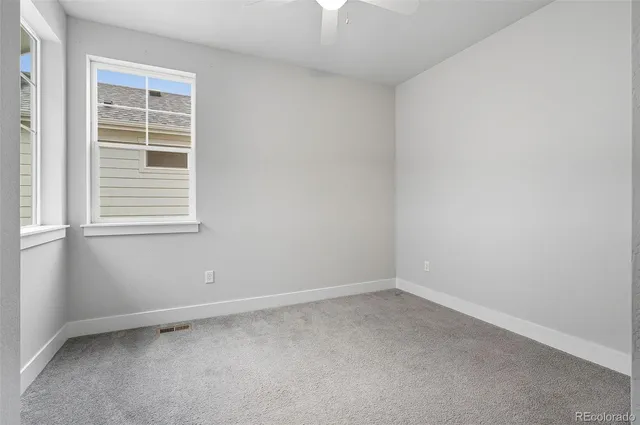 an empty room with chandelier fan and windows