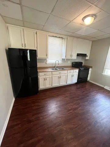 a kitchen with granite countertop a refrigerator a sink dishwasher a stove and white cabinets with wooden floor