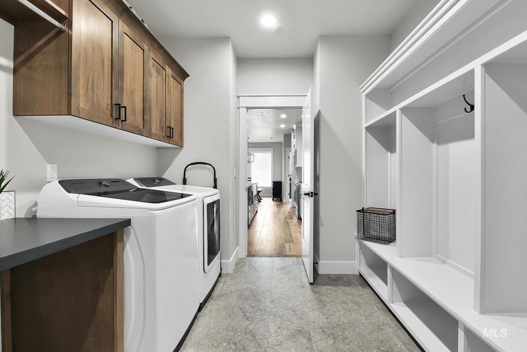 5676 East Zaffre Ridge Street Boise, ID 83716 - Photo 43 of 50 Utility room featuring a built-in white storage system with hooks, concrete-finish flooring, wood-finish cabinetry, dark countertops, and a full-size washer and dryer
