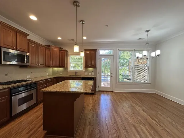 a kitchen with granite countertop wooden floors wooden cabinets a counter top space and stainless steel appliances