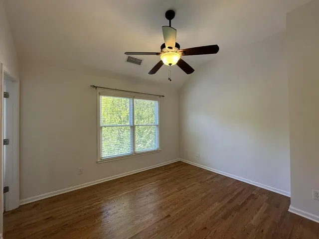 an empty room with wooden floor fan and windows