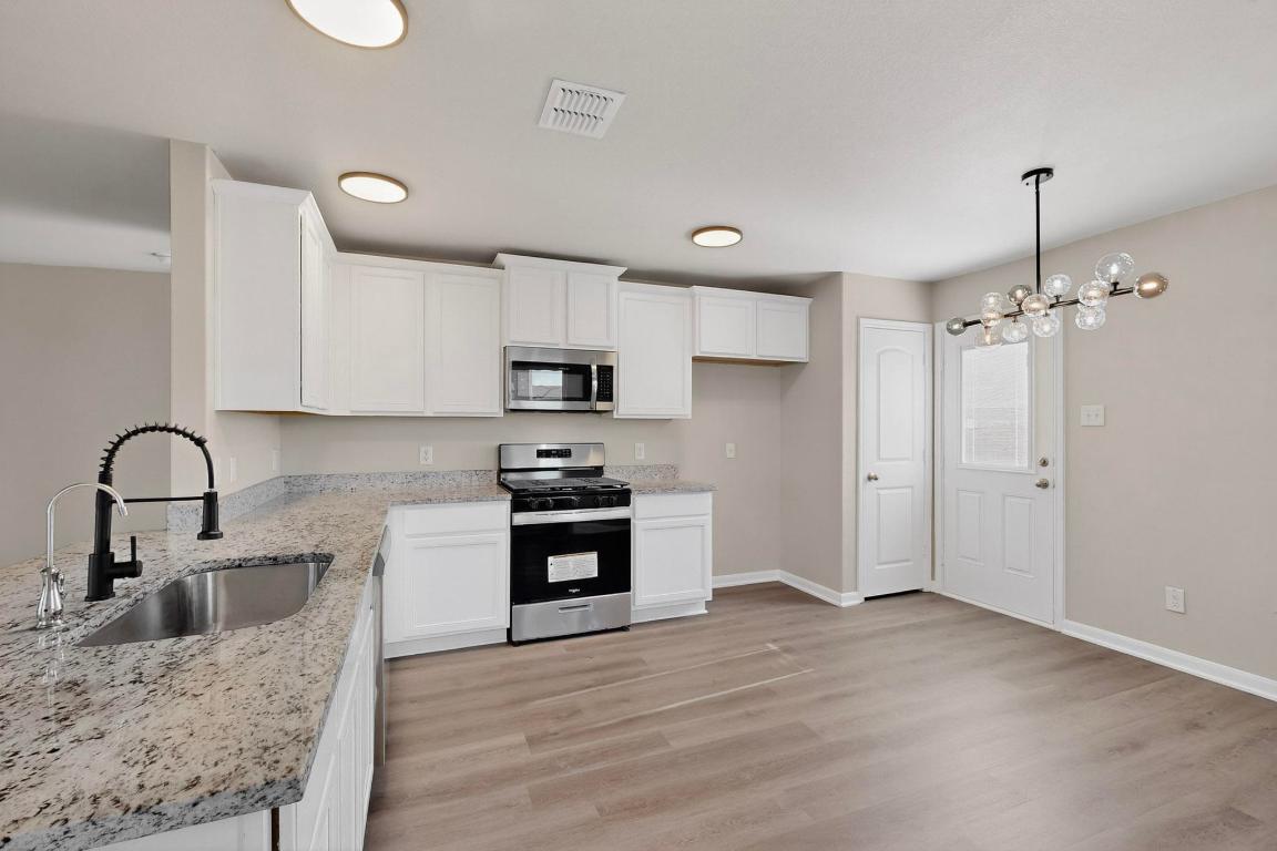 606 Aplite Pass Maxwell, TX 78656 - Photo 12 of 30 Kitchen featuring stainless steel appliances, light wood-style floors, light stone countertops, white cabinetry, and a chandelier