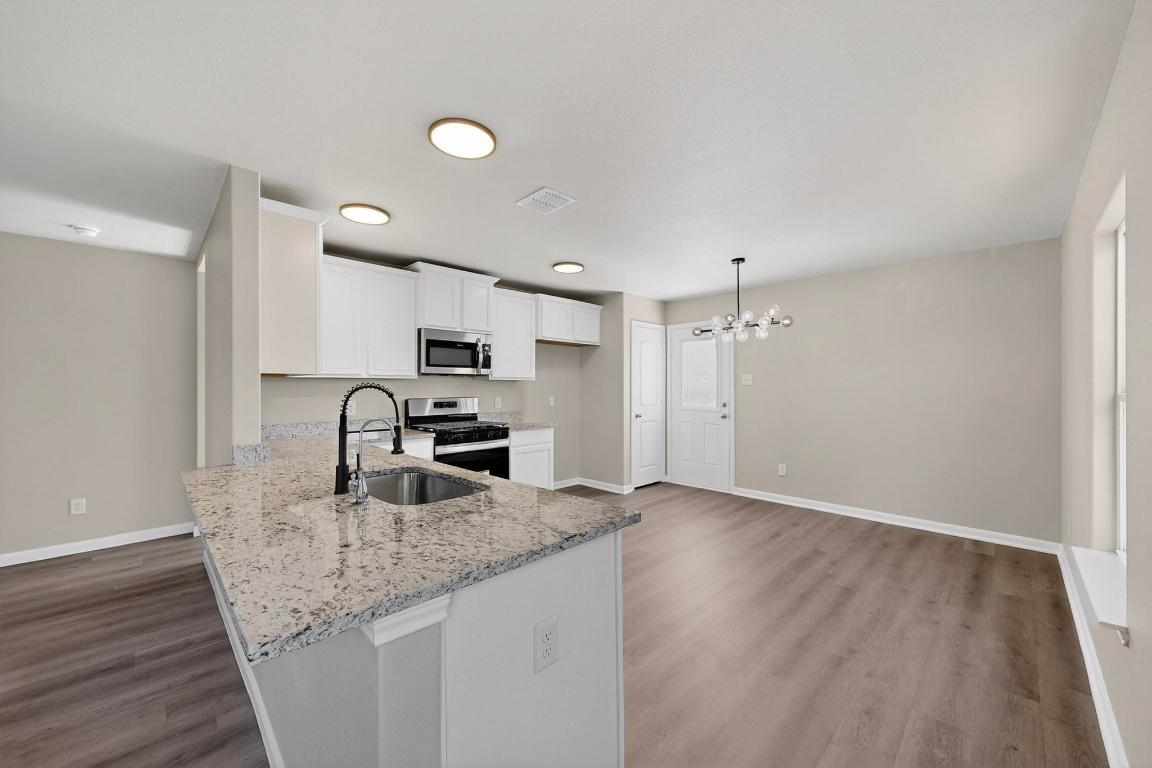 606 Aplite Pass Maxwell, TX 78656 - Photo 8 of 30 Kitchen featuring stainless steel appliances, light stone countertops, white cabinets, a chandelier, and a peninsula