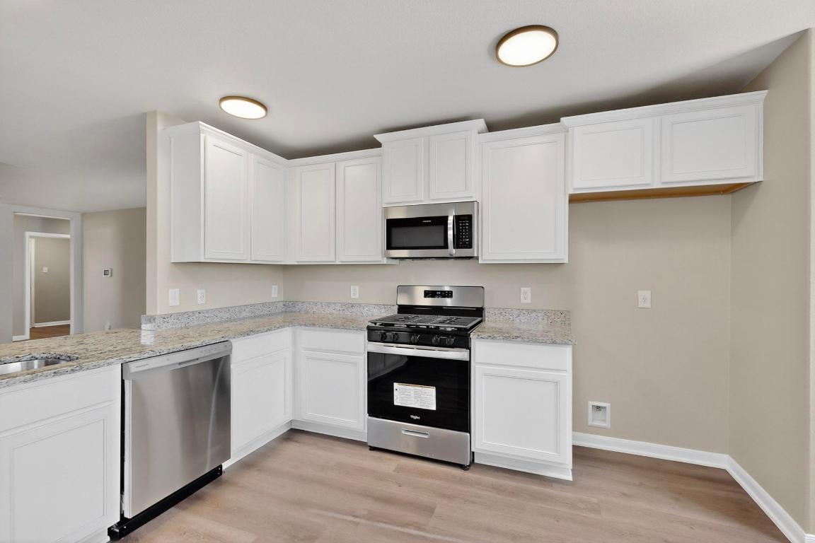 606 Aplite Pass Maxwell, TX 78656 - Photo 9 of 30 Kitchen featuring appliances with stainless steel finishes, light wood-type flooring, light stone counters, and white cabinetry