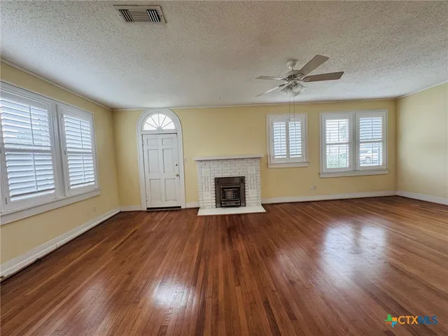 an empty room with wooden floor fireplace and windows