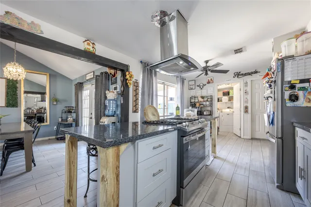 a kitchen with stainless steel appliances granite countertop a refrigerator a sink dishwasher a stove and a dining table with wooden floor