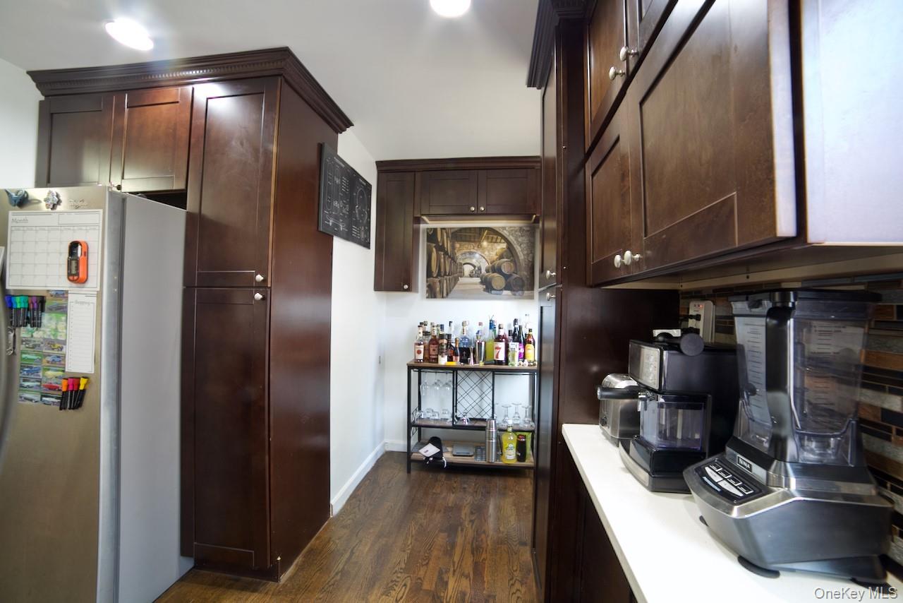 Bar featuring freestanding refrigerator, dark brown cabinetry, dark wood-style flooring, and light countertops
