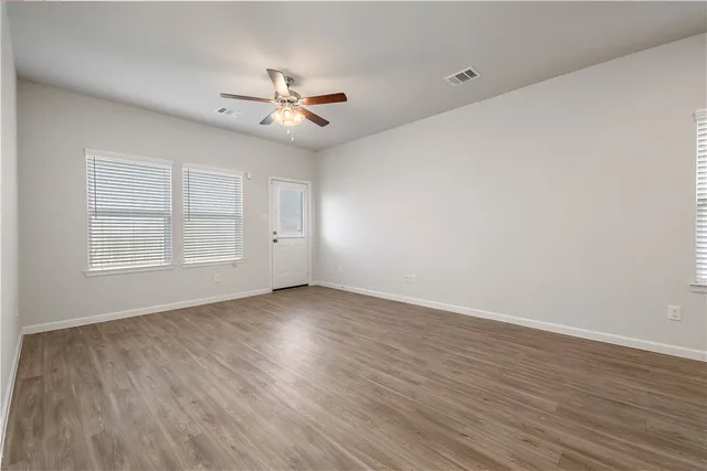 an empty room with wooden floor ceiling fan and windows