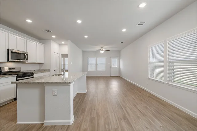 a view of a kitchen with kitchen island a sink wooden floor and stainless steel appliances
