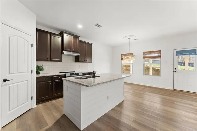 a kitchen with stainless steel appliances granite countertop a stove top oven a sink a refrigerator white cabinets and wooden floor