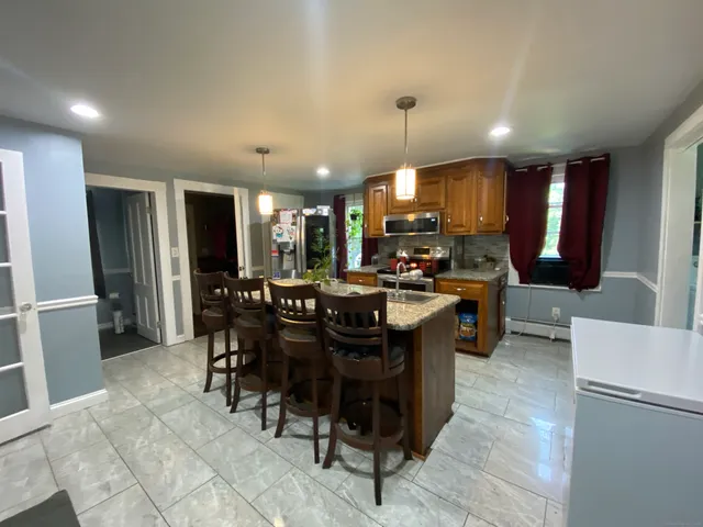 a kitchen with stainless steel appliances kitchen island granite countertop a sink a stove a refrigerator and a dining table with wooden floor