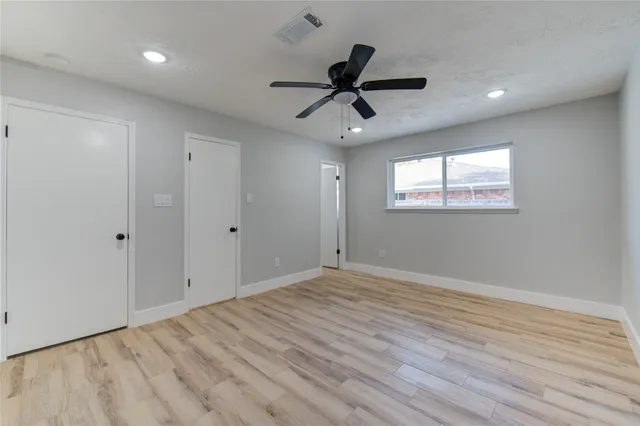 an empty room with wooden floor ceiling fan and windows