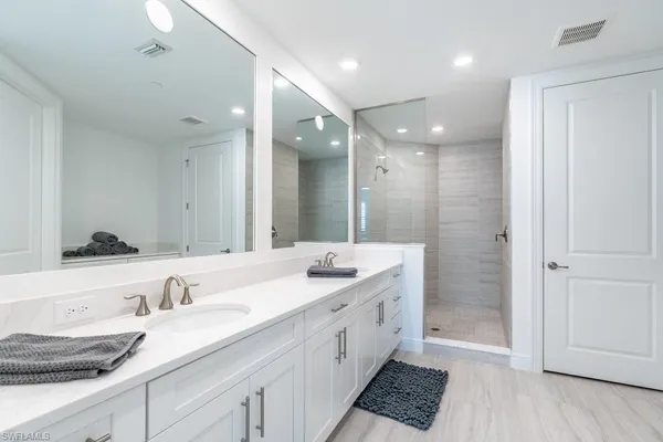a spacious bathroom with a granite countertop double vanity sink a mirror and a shower