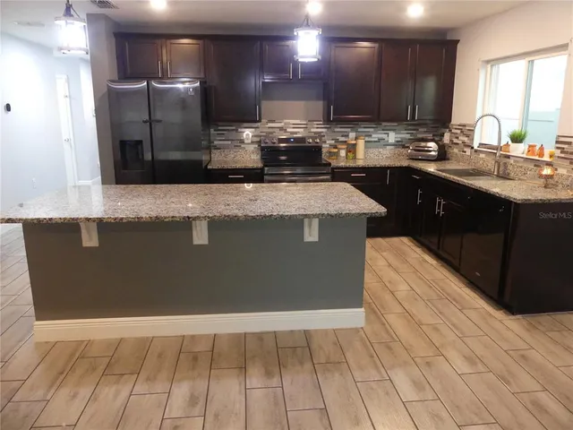 a kitchen with kitchen island granite countertop a sink a counter top space cabinets and stainless steel appliances