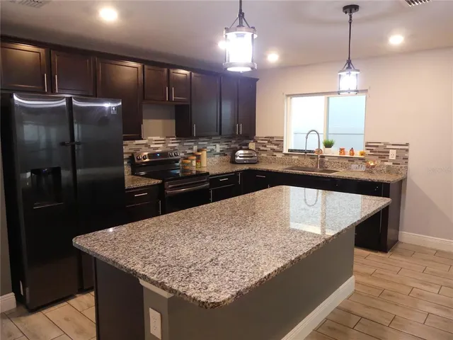a kitchen with kitchen island granite countertop stainless steel appliances a sink stove and refrigerator