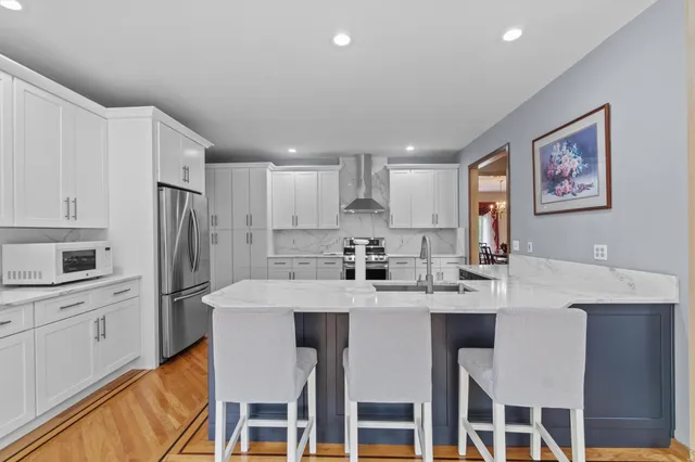 a open kitchen with stainless steel appliances granite countertop a stove top oven a refrigerator a dining table and chairs with wooden floor