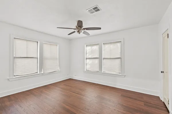 an empty room with wooden floor ceiling fan and windows