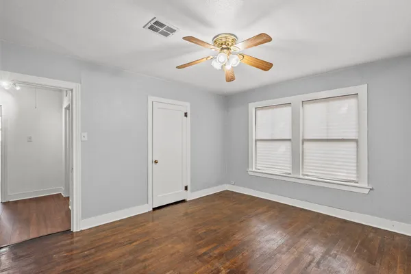 an empty room with wooden floor chandelier fan and windows