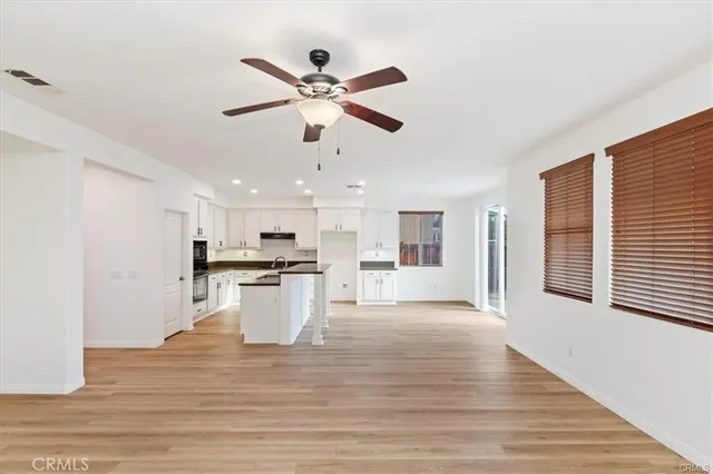 a view of an empty room and kitchen with wooden floor and window