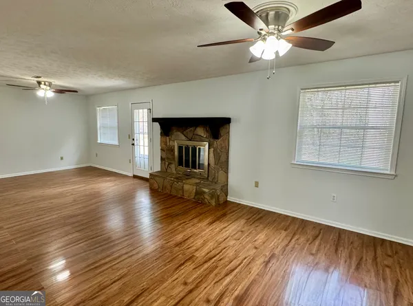an empty room with wooden floor chandelier fan and windows