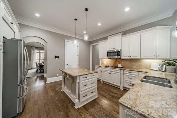 a kitchen with stainless steel appliances granite countertop a refrigerator a sink dishwasher a stove and white cabinets with wooden floor