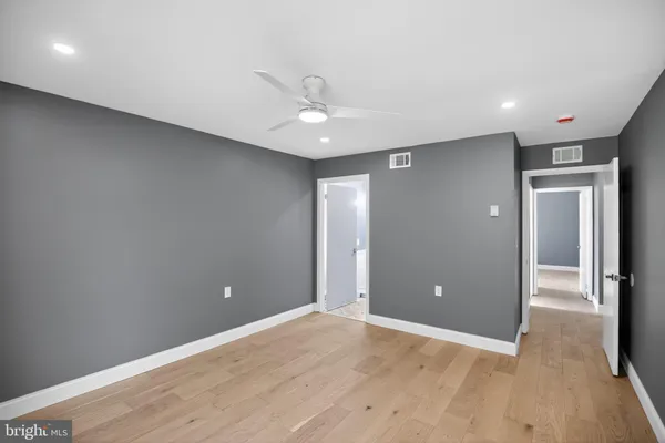 an empty room with wooden floor and way to kitchen