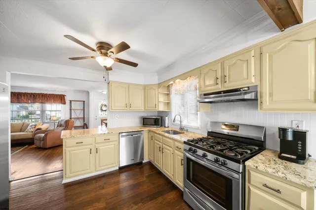 a kitchen with stainless steel appliances granite countertop a stove top oven a sink a dining table and chairs with wooden floor