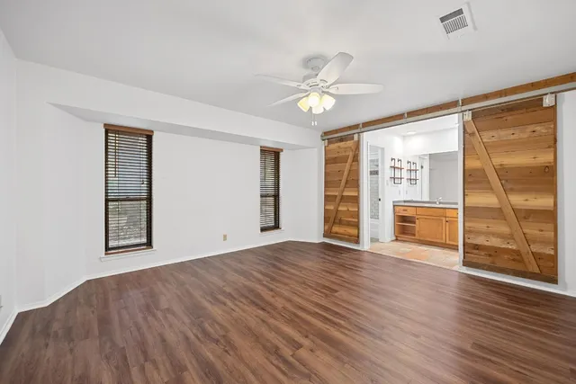 an empty room with wooden floor fan and windows