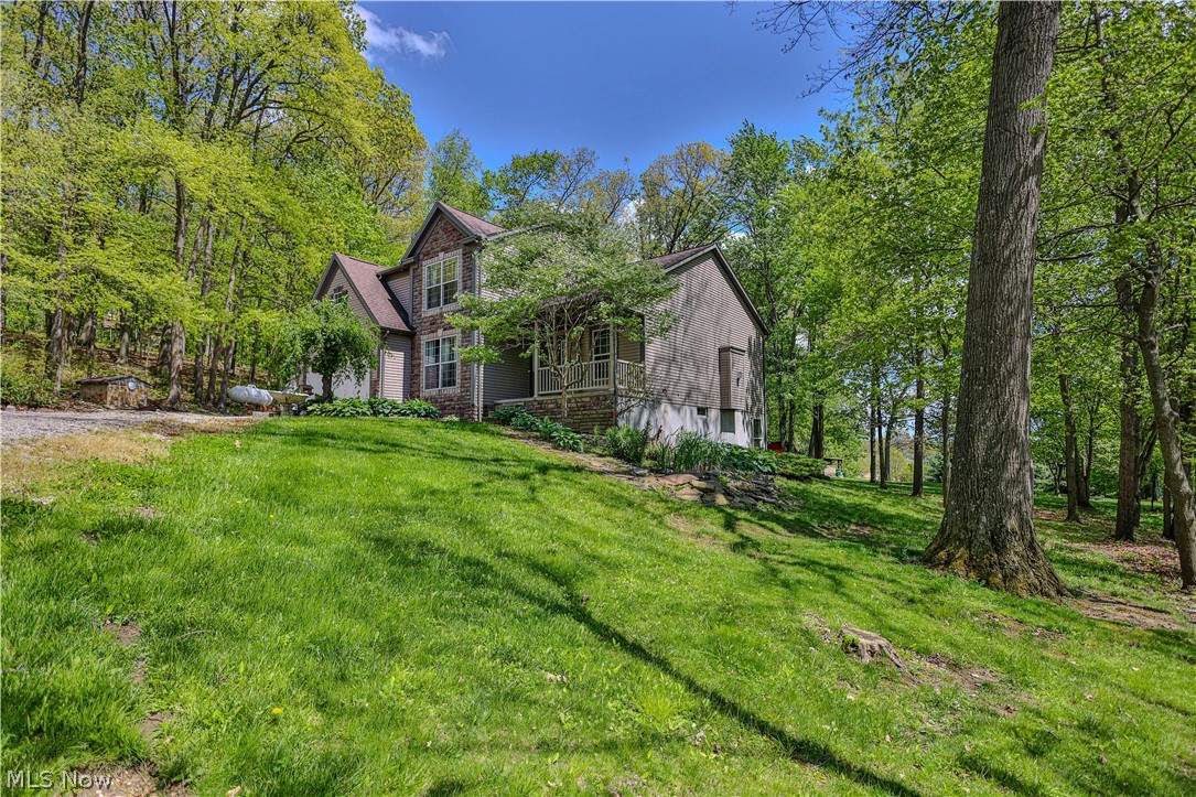 11154 Johnsford Road Southwest Beach City, OH 44608 - Photo 6 of 50 Stone and siding exterior with a covered porch, surrounded by a verdant, wooded landscape and a sloped grassy lawn