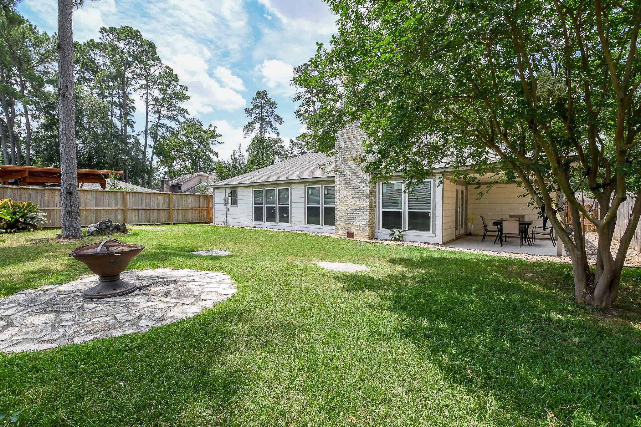 19522 Dianeshire Drive Spring, TX 77388 - Photo 28 of 32 Spacious backyard with a well-maintained lawn, mature trees, and a cozy stone patio featuring a fire pit. The house has large windows and a covered patio area perfect for outdoor dining. Ideal for relaxation and entertaining.