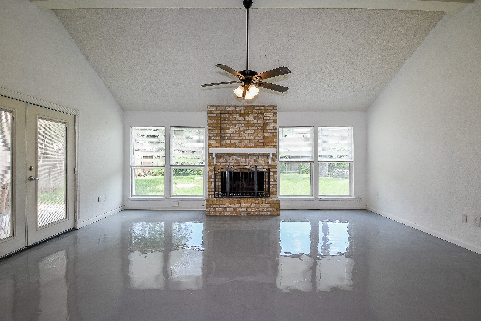 19522 Dianeshire Drive Spring, TX 77388 - Photo 3 of 32 This spacious living room features a high ceiling, a central brick fireplace, and large windows offering ample natural light. The glossy floor adds a modern touch, while the double doors open to the outdoors, enhancing the room's airy feel.