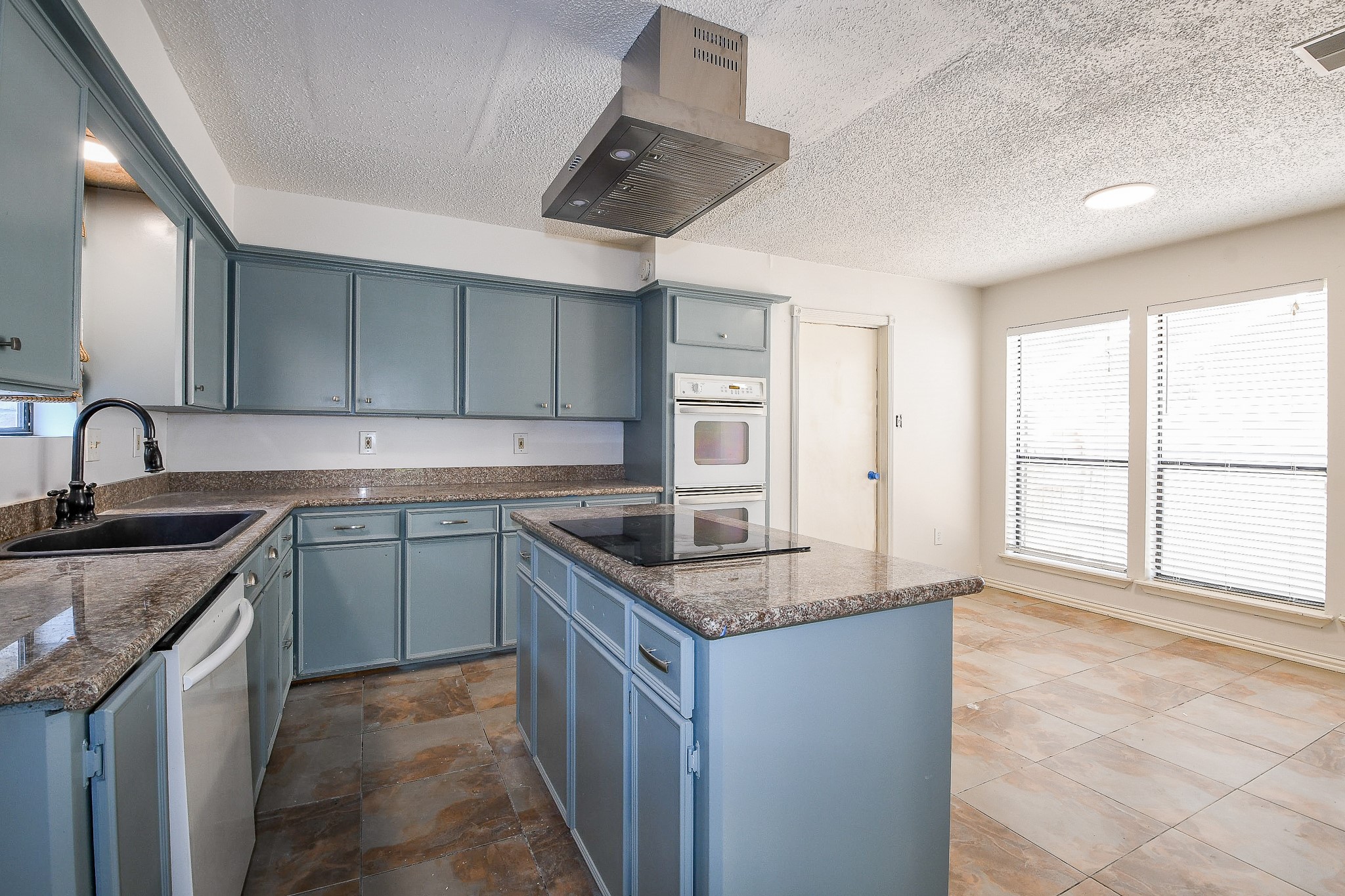 19522 Dianeshire Drive Spring, TX 77388 - Photo 10 of 32 This kitchen features modern blue cabinetry with granite countertops, a central island with an electric cooktop, and a built-in double oven. It has ample natural light from large windows and a spacious layout with tiled flooring.